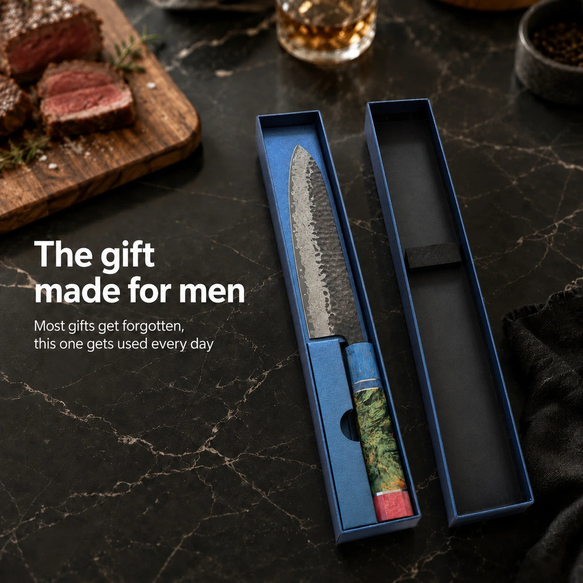A Japanese-style chef's knife with a patterned steel blade and a green-and-red marbled handle, presented in an open blue gift box on a dark marble surface. Sliced steak, a glass of amber liquid, and overlaid marketing text are visible in the scene.