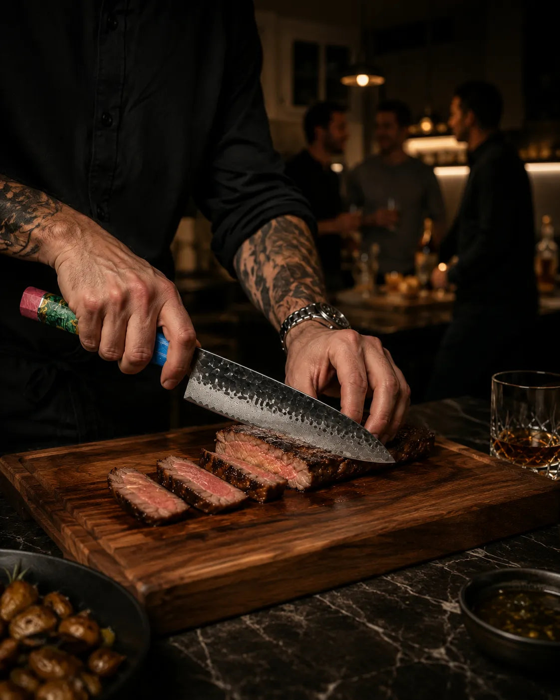 A person with tattooed arms slices a piece of cooked steak on a wooden cutting board in a dimly lit restaurant or bar setting. A glass of amber drink and small bowls sit nearby on a dark marble countertop.