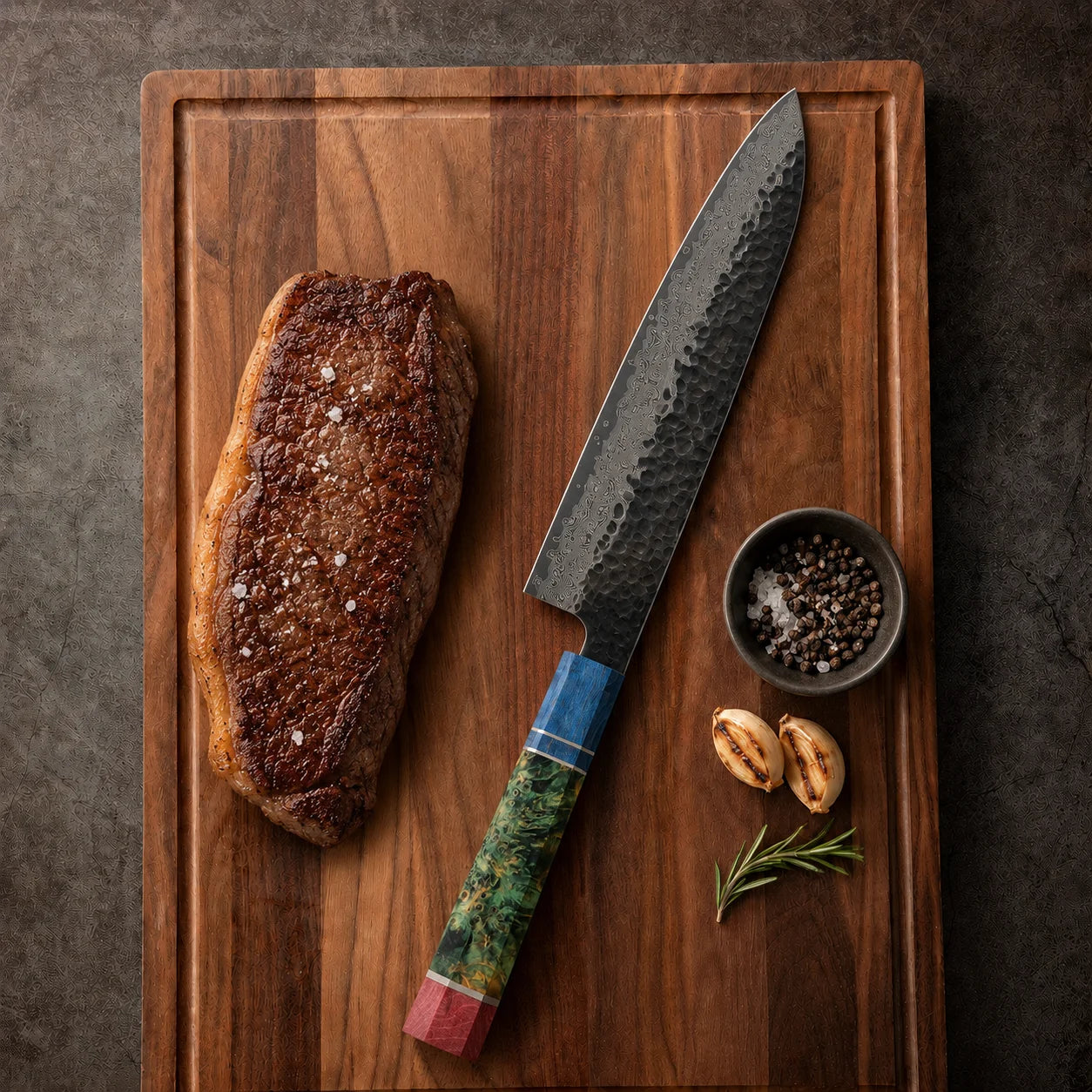 A high-end kori chef's knife with a textured dark steel blade and a colorful, hand-painted wooden handle rests on a wooden cutting board next to a seared steak, a small bowl of peppercorns, and garlic cloves.